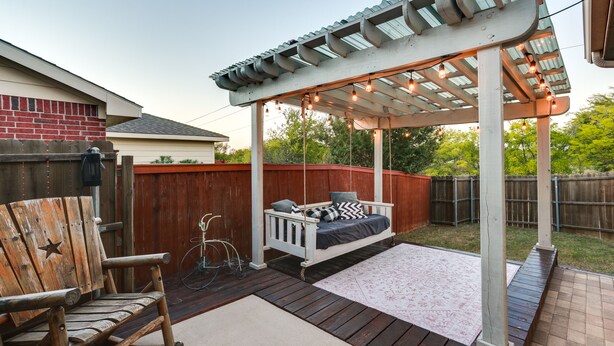 A covered patio area with a swing seat, a wooden rocking chair, and a pergola with string lights. - Patio, Pergola & Pool Access: Aubrey Retreat! (Aubrey)