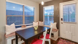 A dining area with a dark wooden table, white chairs with red cushions, and a bench with a patterned cushion. - Patio, Pergola & Pool Access: Aubrey Retreat! (Aubrey)