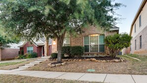 A two-story brick house with a front yard, a small tree, and a pathway leading to the entrance. - Patio, Pergola & Pool Access: Aubrey Retreat! (Aubrey)