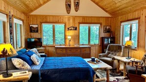 A cozy cabin interior with a large bed, a television, a desk, and a chair.