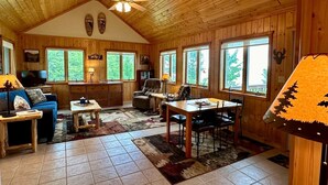 A cozy cabin interior with a dining area, a sofa, a television, and a ceiling fan.