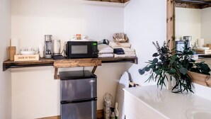 Eine kompakte Küche mit Mikrowelle, Kaffeemaschine und Kühlschrank. Ein Holzregal zeigt ein Schild und diverse Küchenutensilien.