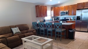 A modern kitchen with wooden cabinets, a stainless steel refrigerator, and a dining area with blue chairs.