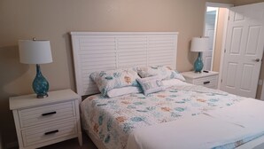 A bedroom with a white bed, floral bedding, two nightstands with lamps, a white dresser, and a door.