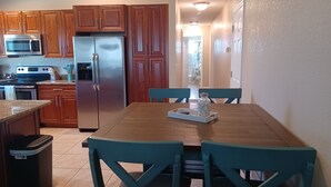 A kitchen with wooden cabinets, a stainless steel refrigerator, a microwave, and a dining table with teal chairs.