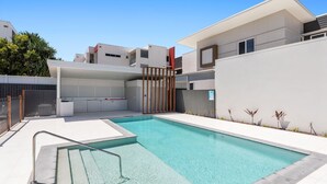 Un área de piscina exterior moderna con una zona de estar cubierta y un acceso mediante portón.