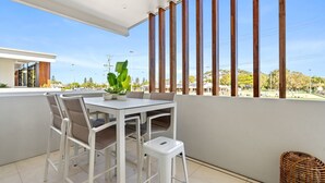 Un balcón con mesa y sillas, una planta en maceta y vistas a una zona residencial con casas y árboles.