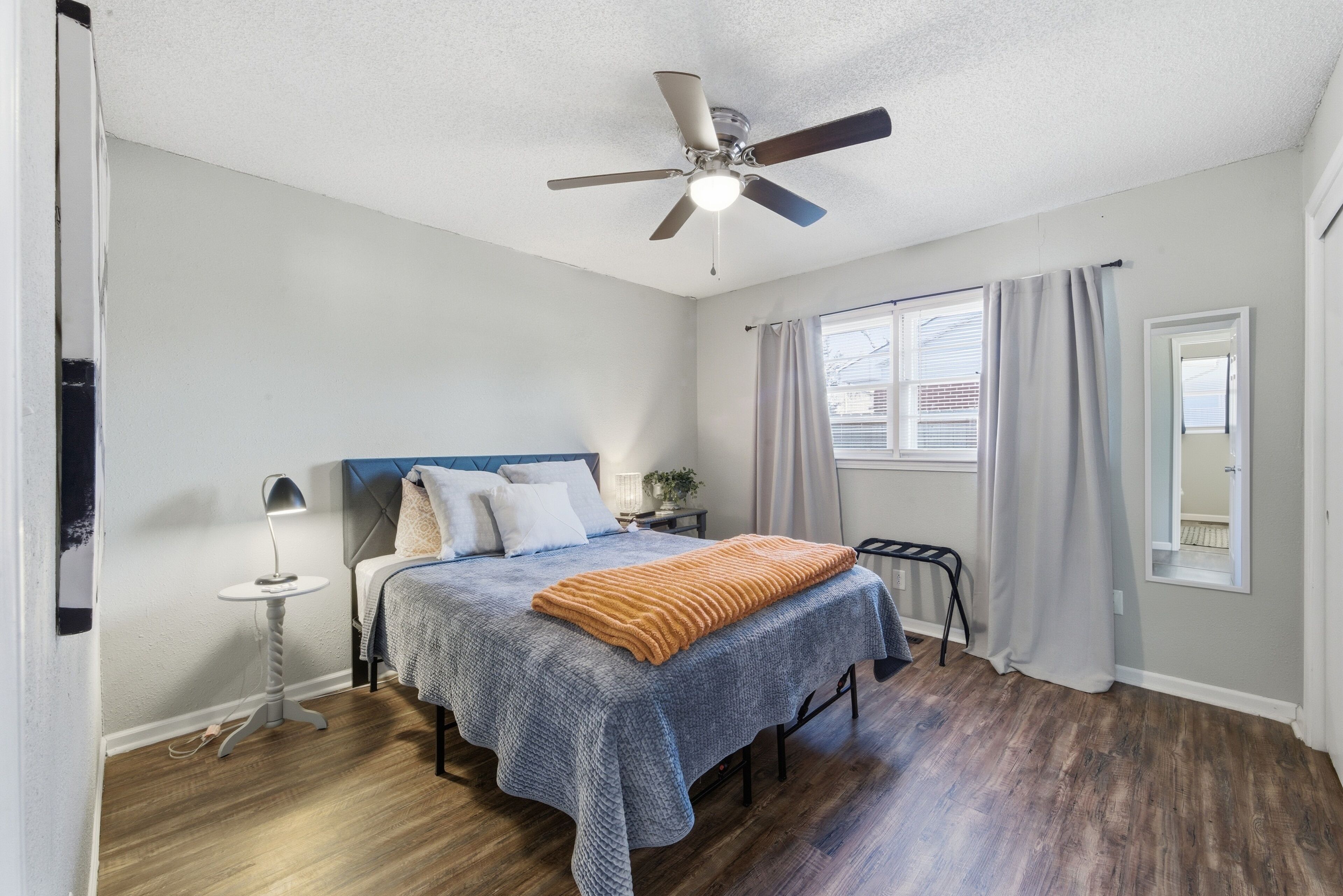 A bedroom with a bed, a ceiling fan, a nightstand, a lamp, and a window with curtains.