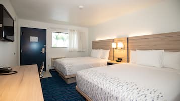 A hotel room with two beds, a desk, a telephone, a window with curtains, and a wall-mounted TV.