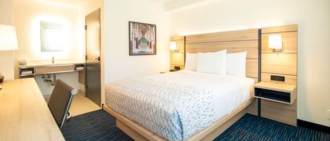 A hotel room with a bed, bedside tables, a desk, and a mirror.