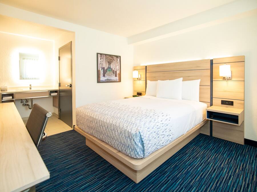 A hotel room with a bed, bedside tables, a desk, and a mirror.