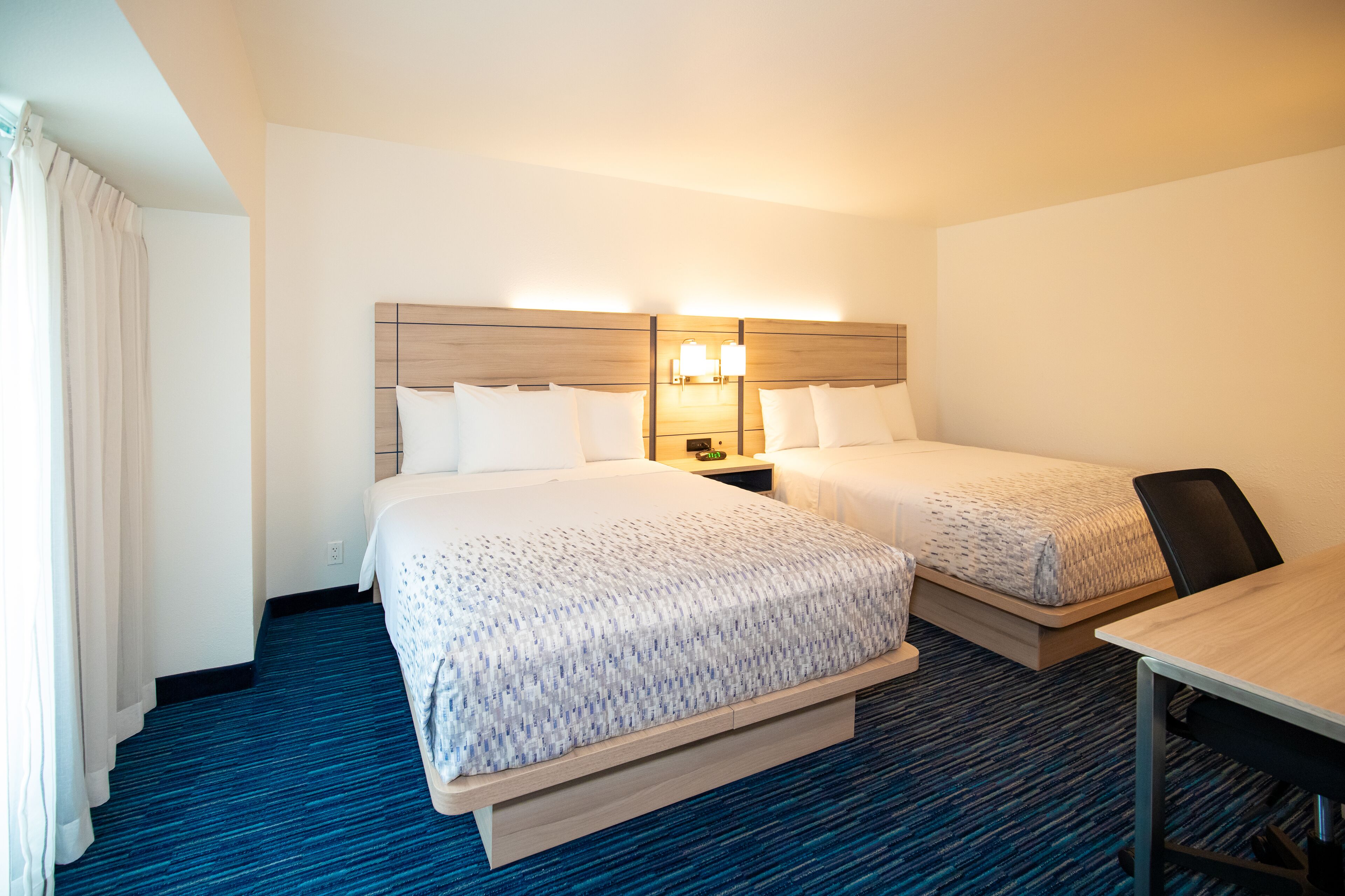 A hotel room with two beds, a desk, and a nightstand with lamps.