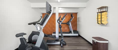 Un gimnasio con dos elípticas, una cinta de correr y un armario de madera.
