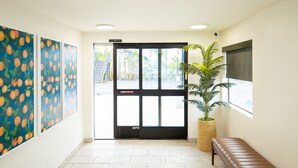 A reception area with a black door, a bench, a potted plant, and a wall with orange fruit paintings. - Orange Grove Inn (Tustin)