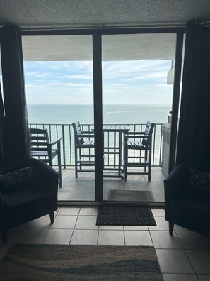 A balcony with a view of the sea, furnished with two chairs and a table.