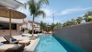 A swimming pool with lounge chairs and umbrellas, a palm tree, and a building with a tiled exterior. - Studio Apartment 'Villa Dionysia 11' with Shared Pool, Wi-Fi and Air Conditioning (Zakynthos)