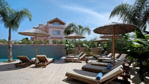 A poolside area with lounge chairs and umbrellas, a building in the background, and a clear sky. - Studio Apartment 'Villa Dionysia 11' with Shared Pool, Wi-Fi and Air Conditioning (Zakynthos)