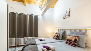 A bedroom with two beds, a window with curtains, a radiator, and a wall-mounted picture.