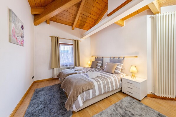 Une chambre à coucher avec un grand lit, une table de chevet avec une lampe, une fenêtre avec des rideaux et un radiateur.