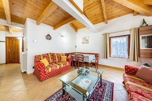 Un salon doté d’un plafond en bois, d’un canapé, d’une table basse en verre et d’un coin repas avec des chaises et une table.