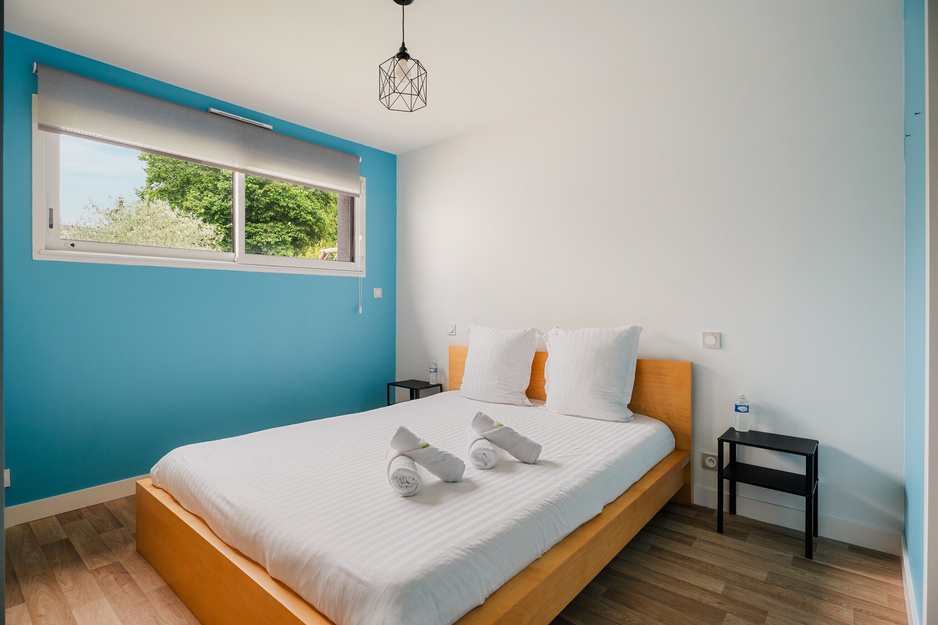 A bedroom with a bed, a window, a nightstand, and a hanging light fixture.