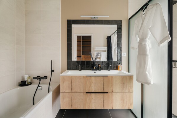 Un baño moderno con tocador de madera, un espejo grande y una bata blanca colgada en un perchero.