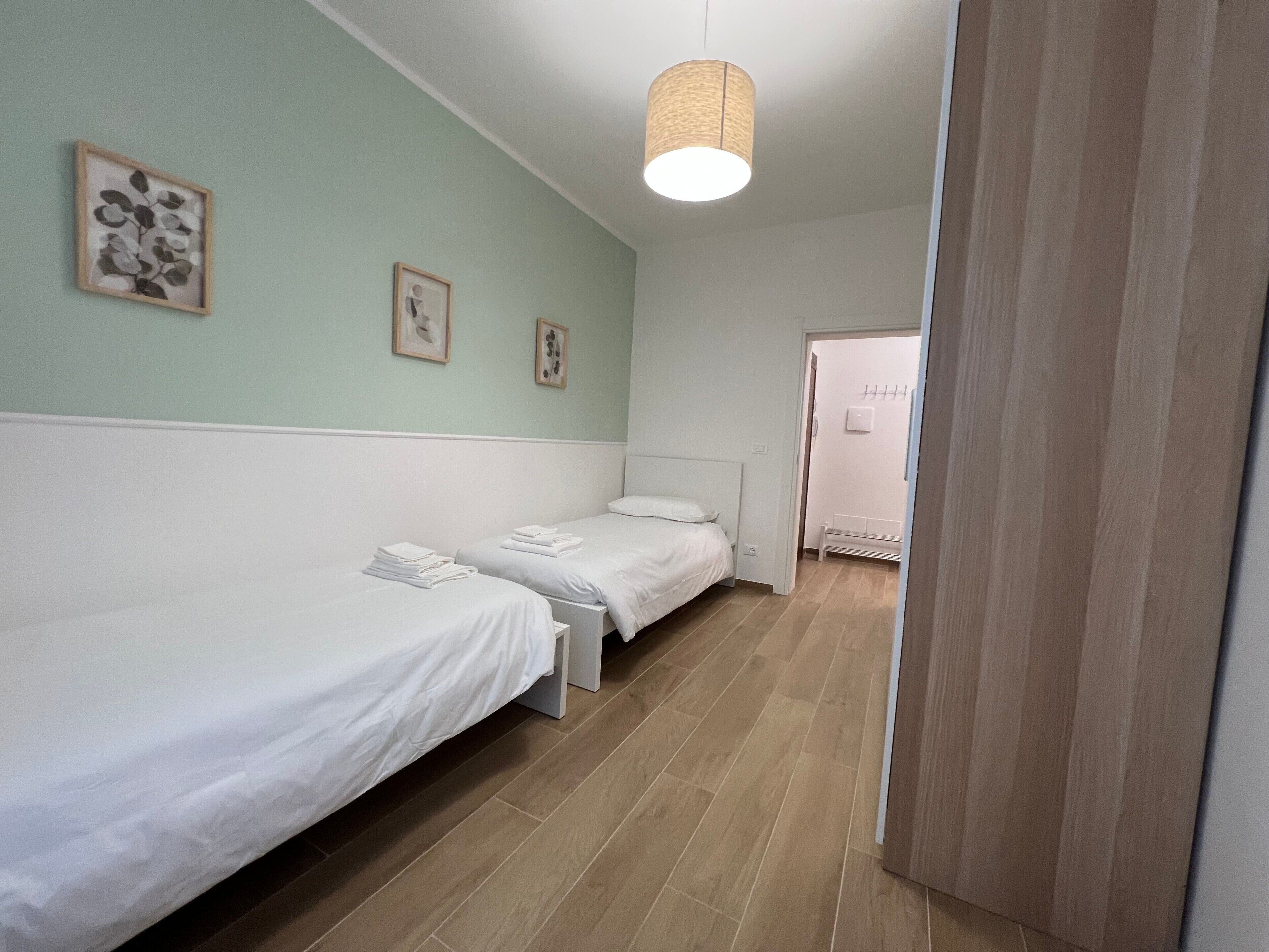A room with two single beds, a hanging light fixture, and a door leading to another room.