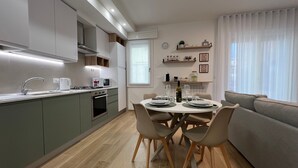 Une cuisine moderne avec un coin repas, comprenant une table dressée pour quatre personnes, un canapé et une fenêtre avec des stores.