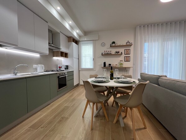 A modern kitchen with a dining area, including a table set for four, a sofa, and a window with blinds.