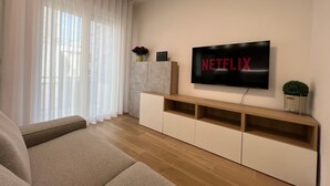 Un salon avec un téléviseur à écran plat fixé au mur, un canapé, un meuble en bois et une plante en pot.