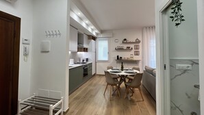 Une cuisine moderne dotée d’appareils électroménagers intégrés, un coin repas avec une table et des chaises, et un couloir avec un banc.