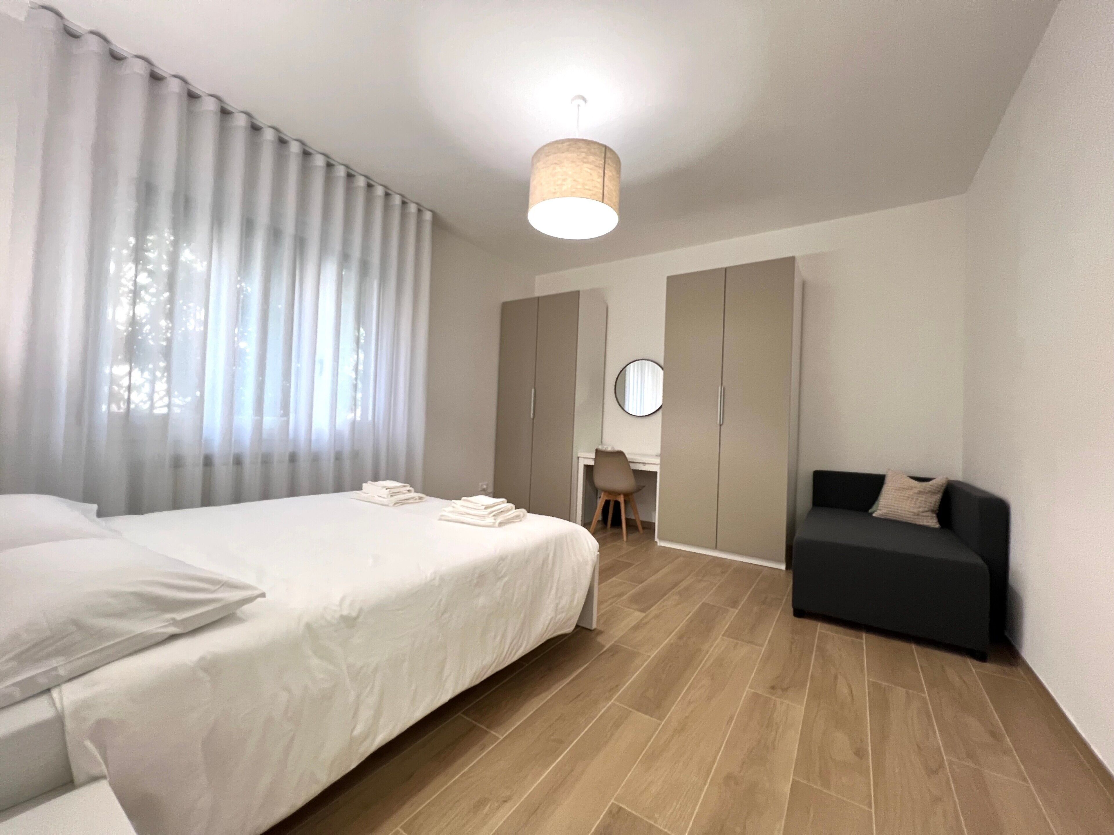 A bedroom with a bed, a desk, a wardrobe, a sofa, and a hanging light fixture.