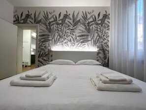 A bedroom with a large bed, white linens, a headboard with a leaf pattern, and a view of a bathroom.