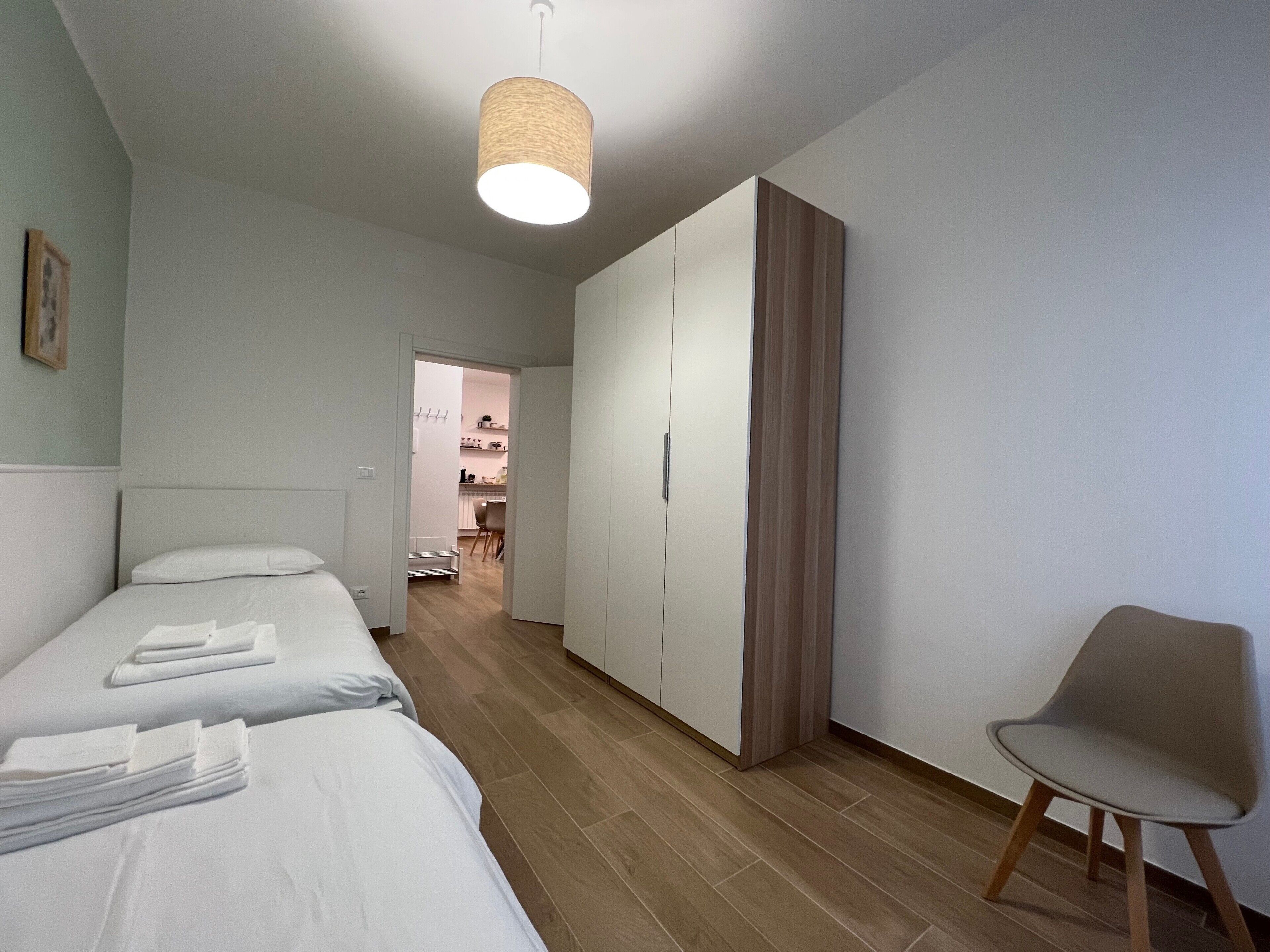 Quarto de hotel com cama, uma cadeira, um guarda-roupa e um candeeiro suspenso.