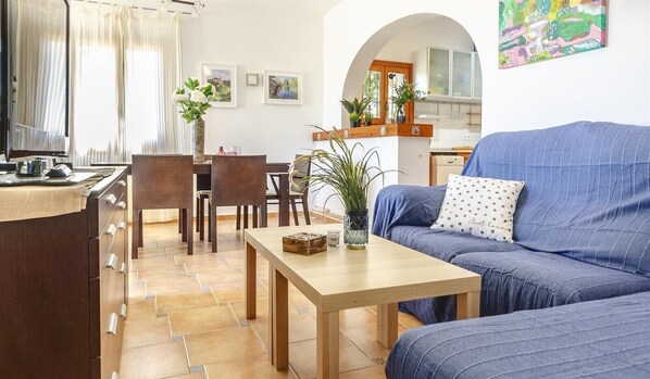 Una sala de estar con sofá, mesa de centro, mesa de comedor, sillas y una cocina con ventanal.