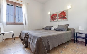 Un dormitorio con cama, dos almohadas, una silla, una mesita de noche, una lámpara y dos luces empotradas en la pared.