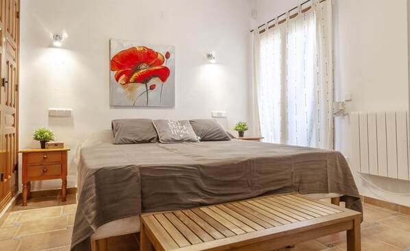 Un dormitorio con cama, mesitas de noche, un banco, un cuadro y un radiador.
