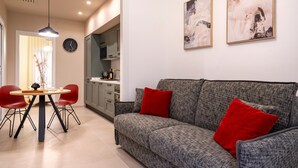 Ein modernes Wohnzimmer mit grauem Sofa, roten Kissen, einem Esstisch mit Stühlen und abstrakten Wandbildern.