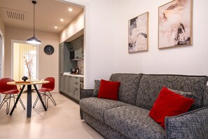 A modern living room with a grey sofa, red cushions, a dining table with chairs, and abstract wall art. - Apartment "Dimora Màufra" with Wi-Fi & A/C (Locorotondo)