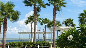 Eine Küstenlandschaft mit Palmen, einem weißen Kiosk und Blick aufs Meer.