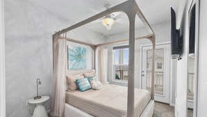 Ein Himmelsbett mit Baldachin, ein Deckenventilator, ein kleiner Nachttisch und eine dekorative Wanddekoration.