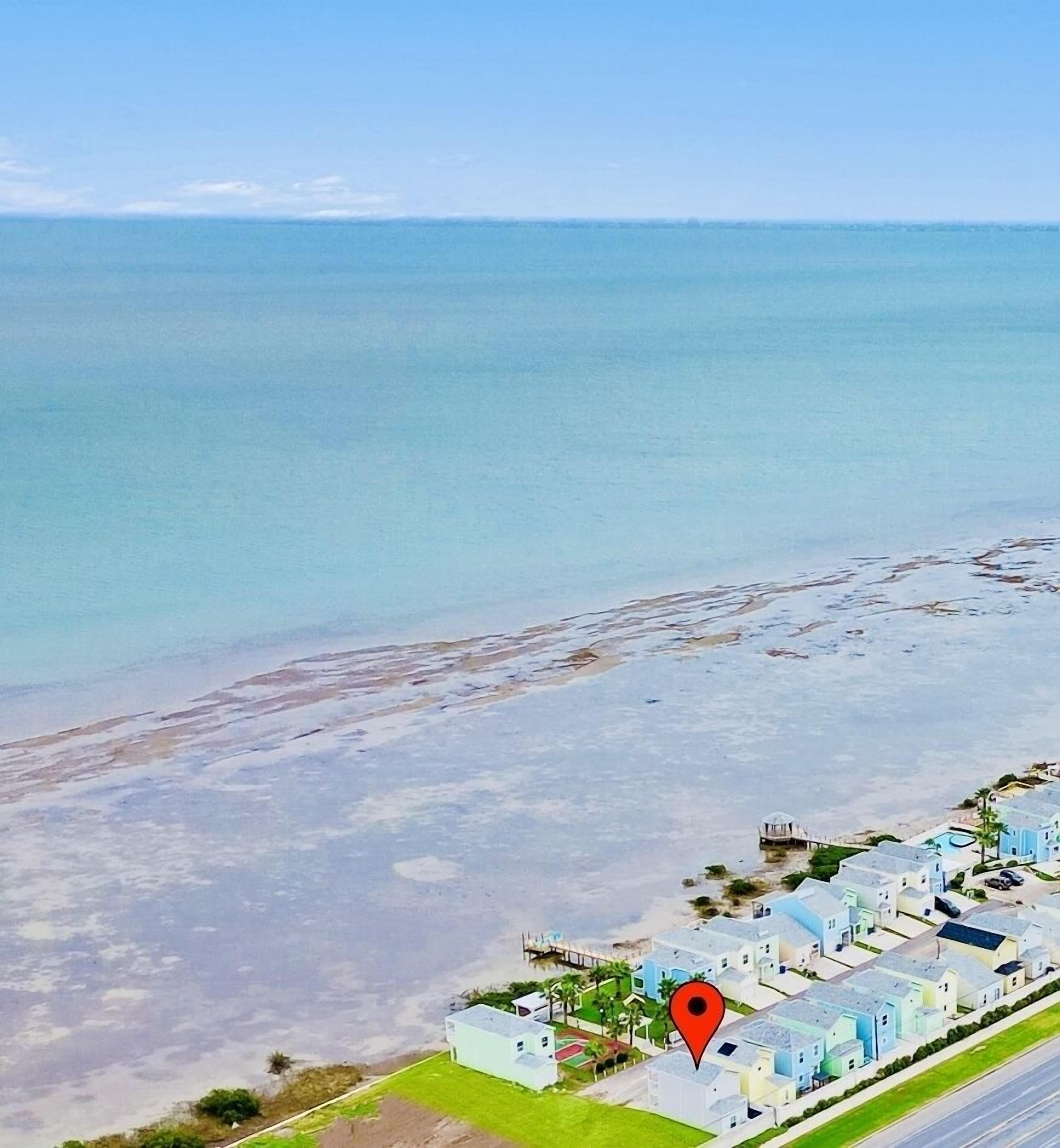 An aerial view of a coastal area with a row of light-colored buildings adjacent to a beach.