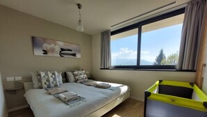 Un dormitorio con cama, ventana con cortinas, mesita de noche y una obra de arte en la pared.