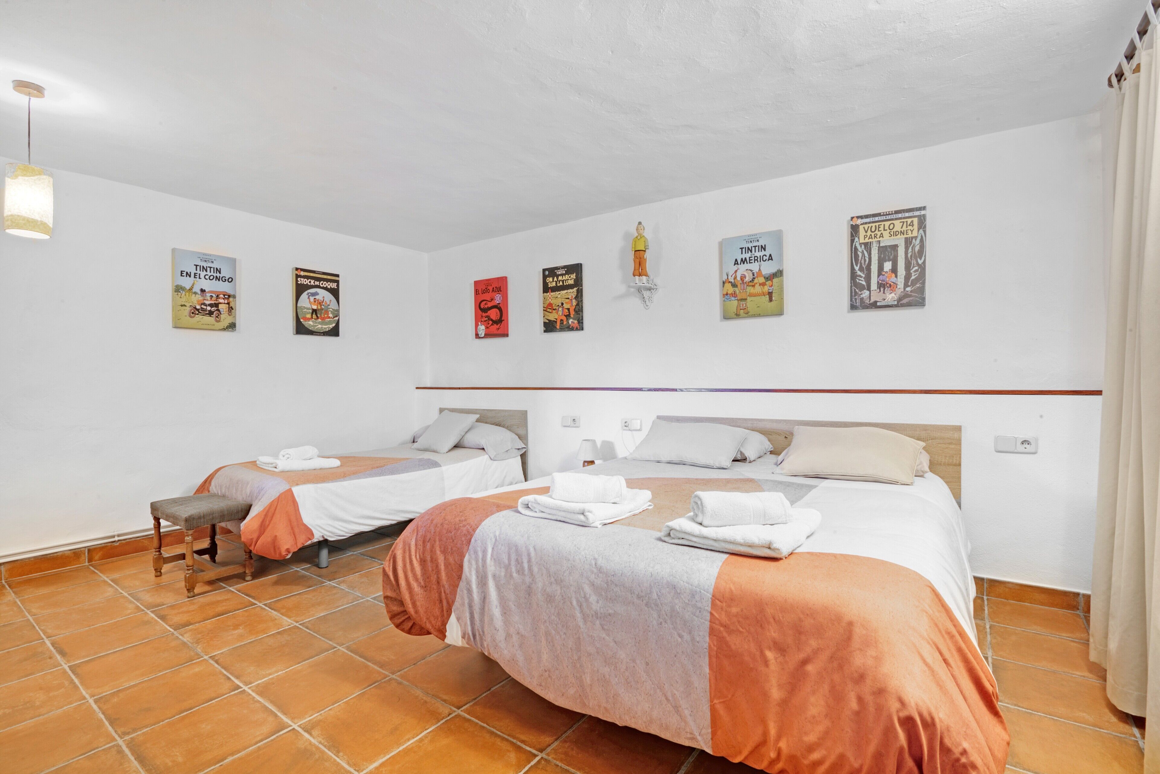 Una habitación de hotel con dos camas, un banco y una pared decorada con carteles.