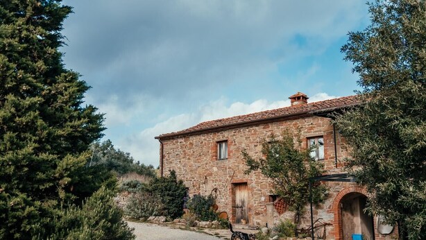 Un bâtiment en pierre à l’aspect rustique, une allée de gravier et un chien qui se promène à proximité.