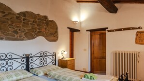Une chambre avec deux lits, un mur en pierre, une porte en bois, un radiateur et une table de chevet avec une lampe.
