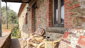 Un bâtiment en pierre doté d’un balcon, de meubles en osier et de deux verres de vin rouge.