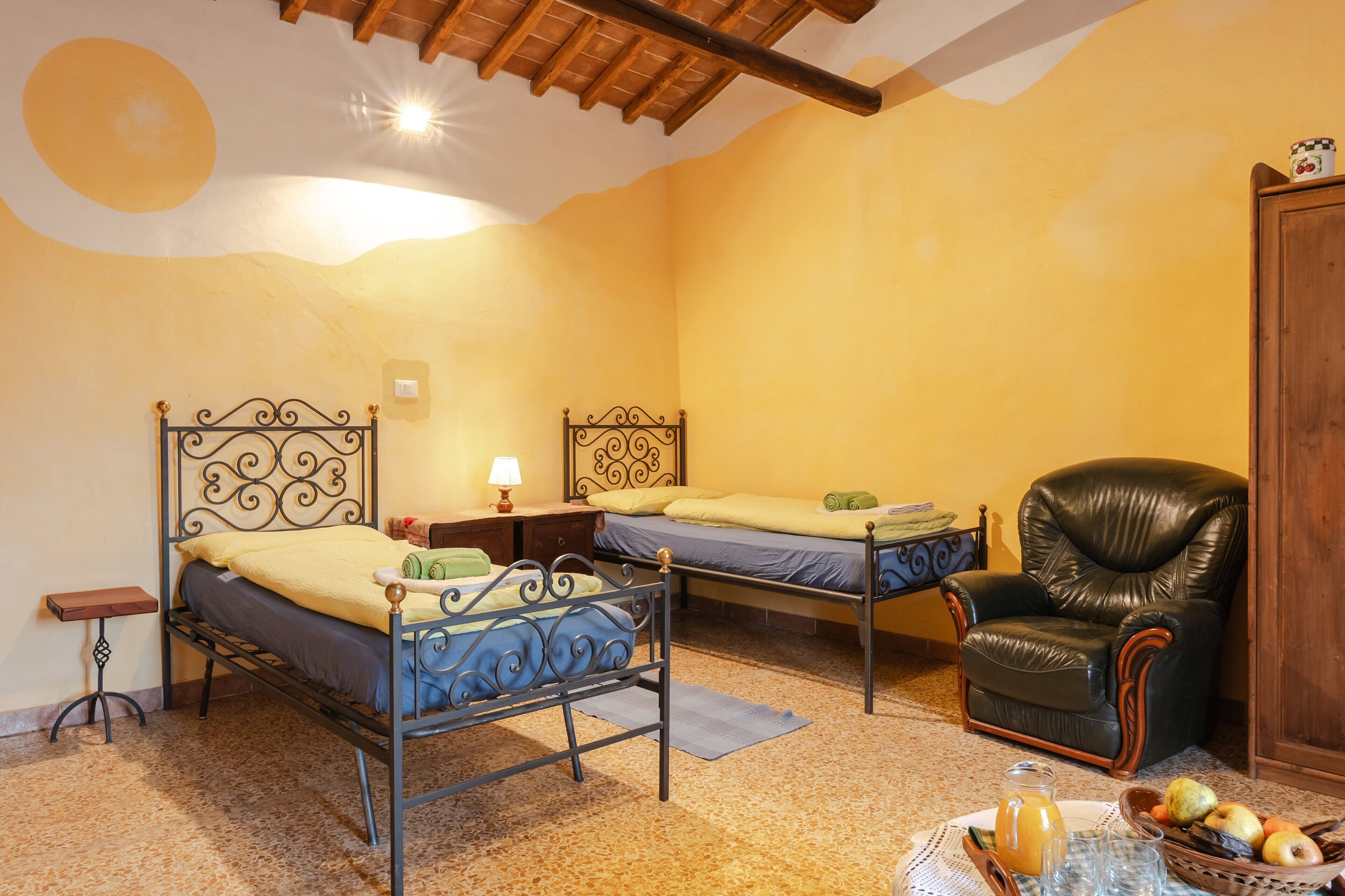 Une chambre avec deux lits, une chaise, une table avec des fruits et une lampe.