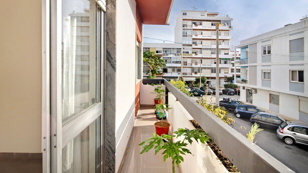 A balcony with potted plants, a view of a street with parked cars, and adjacent buildings. - Apartment 'Matinhos House' with Balcony, Wi-Fi and Air Conditioning (Faro)