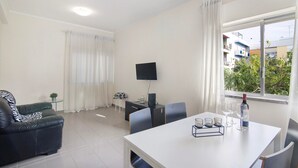 A modern living room with a sofa, a dining table with chairs, a TV, and a window with curtains. - Apartment 'Matinhos House' with Balcony, Wi-Fi and Air Conditioning (Faro)